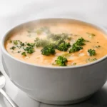 A bowl of smooth broccoli cheddar soup garnished with parsley.